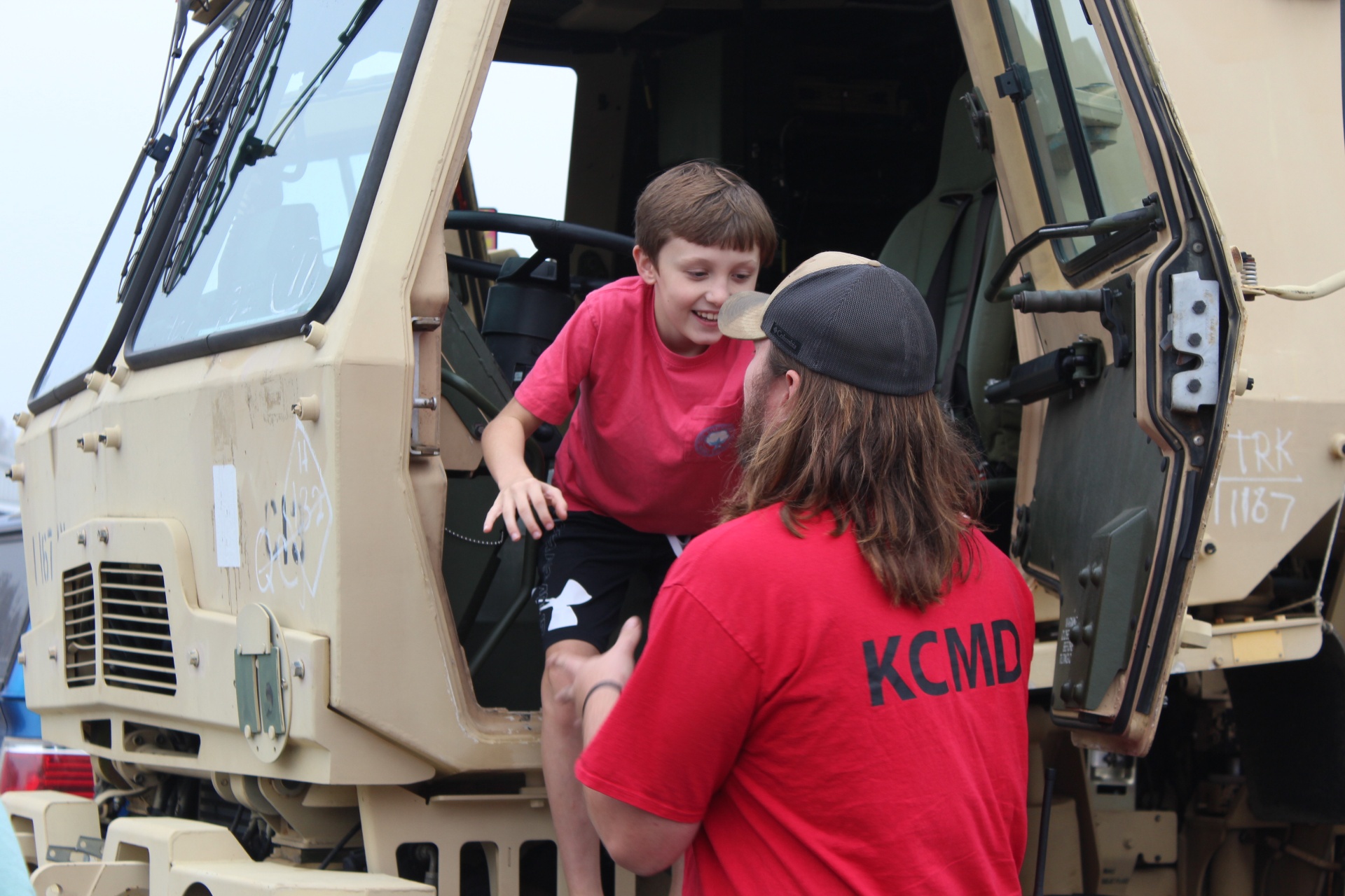 KCMD volunteer helps a young visitor climb down from a military truck