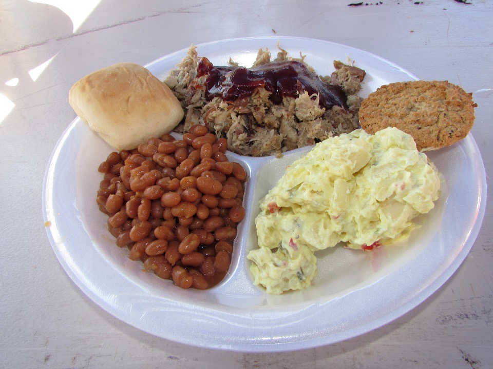 Plate of pulled pork with baked beans, potato salad, and a roll
