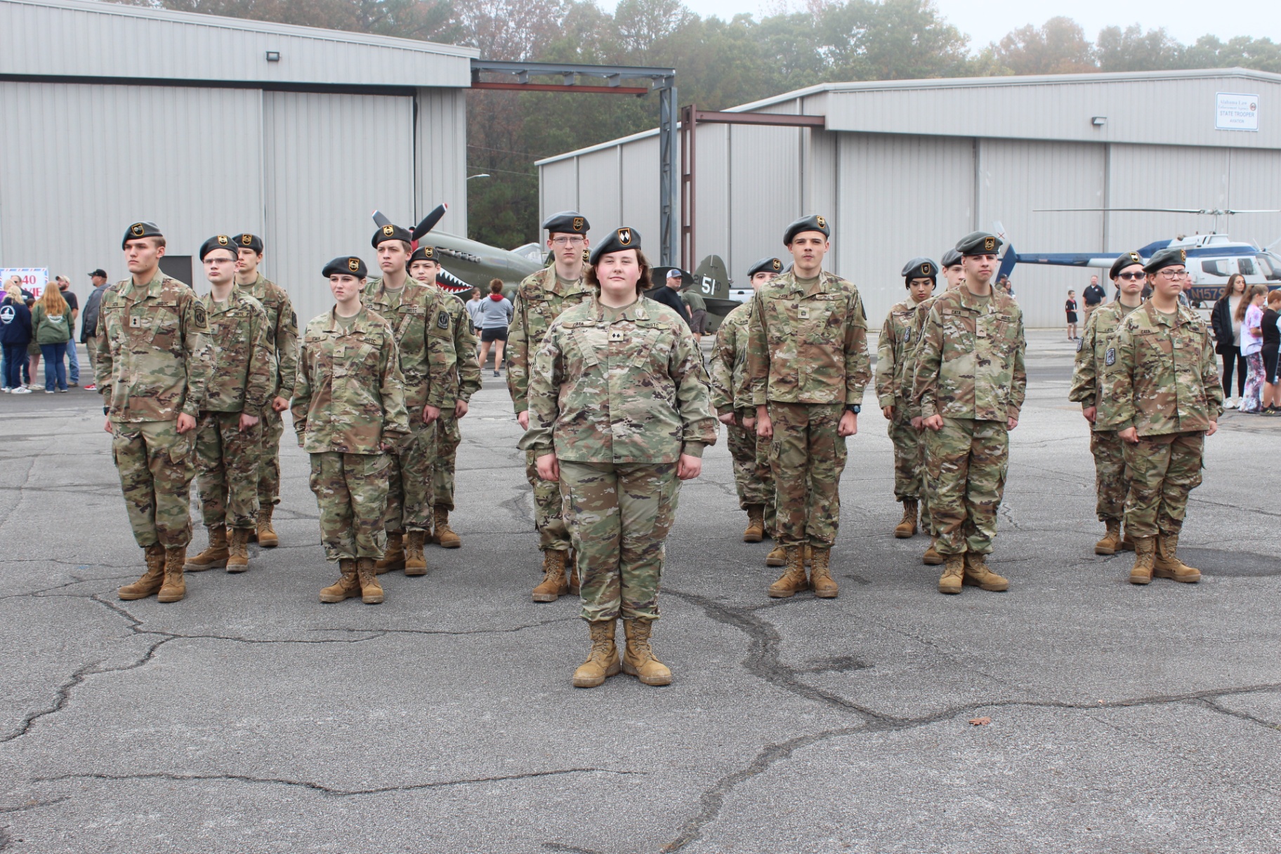 JROTC cadets stand in formation on the tarmac with warbirds behind